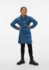 Vidutinio mėlynumo džinsinis suknelė su koloriniu apykakle, priekyje užsegama mygtukais ir kišene. Derinama su juodomis leggings ir auliniais batais su storiais padu.