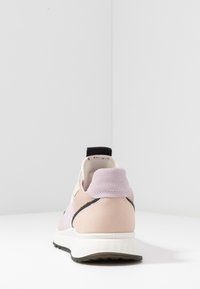 Sneaker con tomaia in suede rosa pastello e lavanda, dettagli neri, collo imbottito e suola bianca testurizzata. La vista posteriore mostra i dettagli delle cuciture.