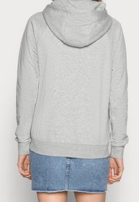 Sudadera gris con capucha, mangas raglán, tejido texturizado y un bolsillo tipo canguro. Combinada con una falda de mezclilla, mostrando un atuendo casual.
