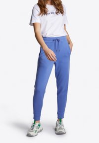 Pantalones de chándal azul claro con cintura ajustable, bolsillos laterales y puños acanalados, combinados con una camiseta blanca con estampado en azul marino.