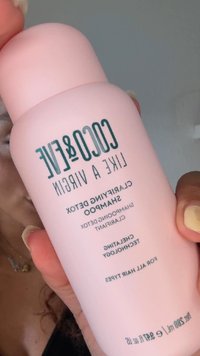 Main tenant une bouteille rose de shampooing Coco & Eve Like a Virgin Clarifying Detox avec texte visible et fond neutre.