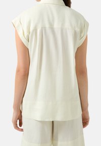 Camicetta senza maniche di un giallo chiaro con colletto e una sottile trama. Caratterizzata da una spalla sul retro e un taglio dritto, abbinata a pantaloni coordinati.