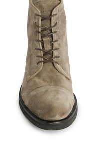Stivaletto in suede beige con punta tondeggiante, caratterizzato da lacci marroni scuri, una superficie testurizzata e una suola in gomma nera.