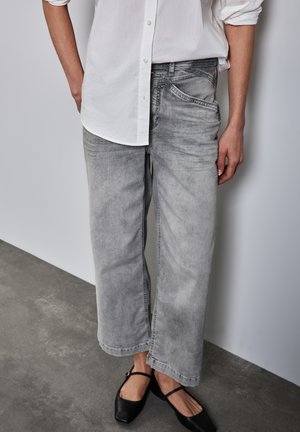 Jeans a gamba larga grigio chiaro realizzati in denim, con una leggera sfumatura, un classico design a cinque tasche e una vestibilità rilassata abbinati a una camicia bianca.