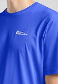 T-shirt bleu royal en tissu lisse, arborant un petit logo Jack Wolfskin blanc sur le côté gauche. Manches courtes, col rond.