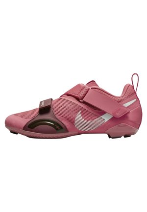 Różowy but sportowy z dwoma regulowanymi paskami i białym logo Nike Swoosh po boku na białym tle.