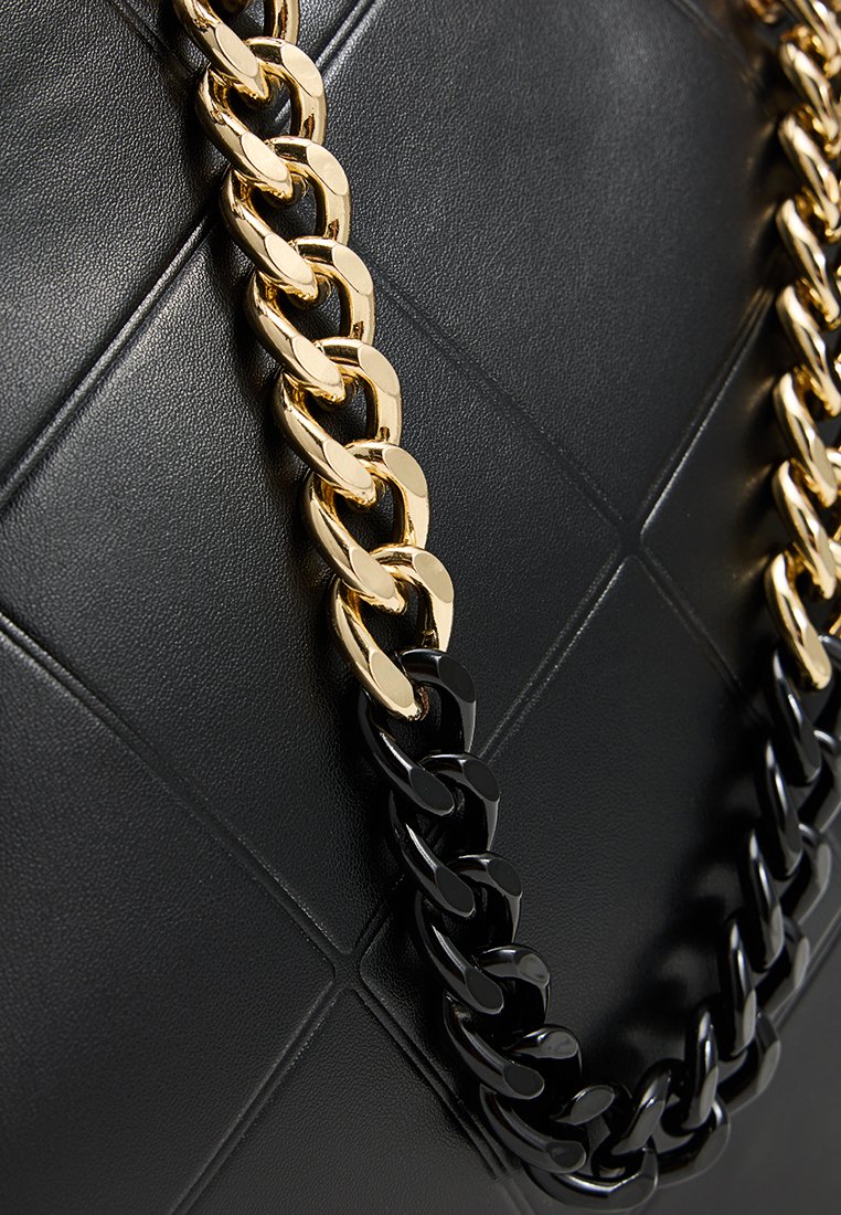 Surface en cuir matelassé noir avec des détails en chaînes en métal doré et noir entrelacées.