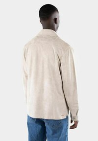 Giacca in suede beige con un fit rilassato, caratterizzata da un colletto a punta, maniche lunghe e un accento di logo arancione vicino all'orlo.