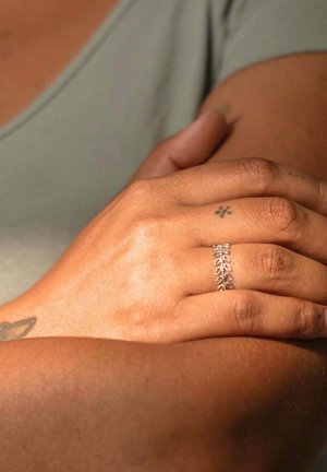Anello d'argento con un delicato design a foglia, indossato su una mano con tono di pelle abbronzato. La mano poggia su un altro braccio, mostrando una leggera texture e dettagli.