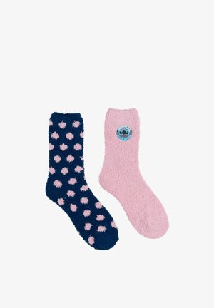 One navy sock with pink polka dots and one pink sock featuring a small blue cartoon character patch. Both are fuzzy.