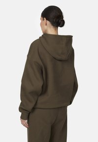 Sweatshirt à capuche marron avec une coupe décontractée, présentant une texture douce et des poignets côtelés, vu de l'arrière. Aucun logo ni motif visible.