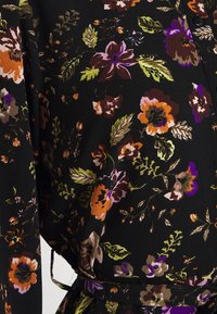 Tissu noir avec imprimé floral orange, violet et marron ainsi que des feuilles vertes, avec un bouton et une ceinture en tissu assortie.