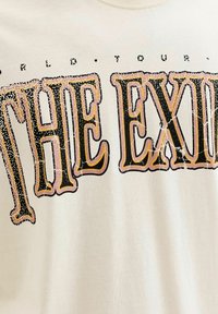 Κείμενο σε ρετρό στυλ "THE EX" με έντονα μαύρα και ροζ γράμματα με λευκές κηλίδες σε εκρού ύφασμα, μέρος μεγαλύτερης εκτυπωμένης φράσης.