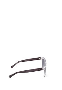 Gafas de sol rectangulares transparentes con brazos de plástico marrón oscuro. Presentan lentes claros y el logo grabado "GUESS" en las patillas.