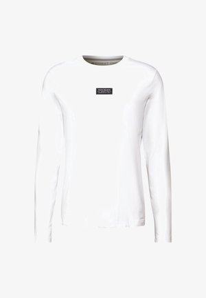 Biała, długorękawowa koszulka z bawełny, z prostokątną czarną metką z białym napisem na klatce piersiowej. Gładka tekstura i luźny krój.