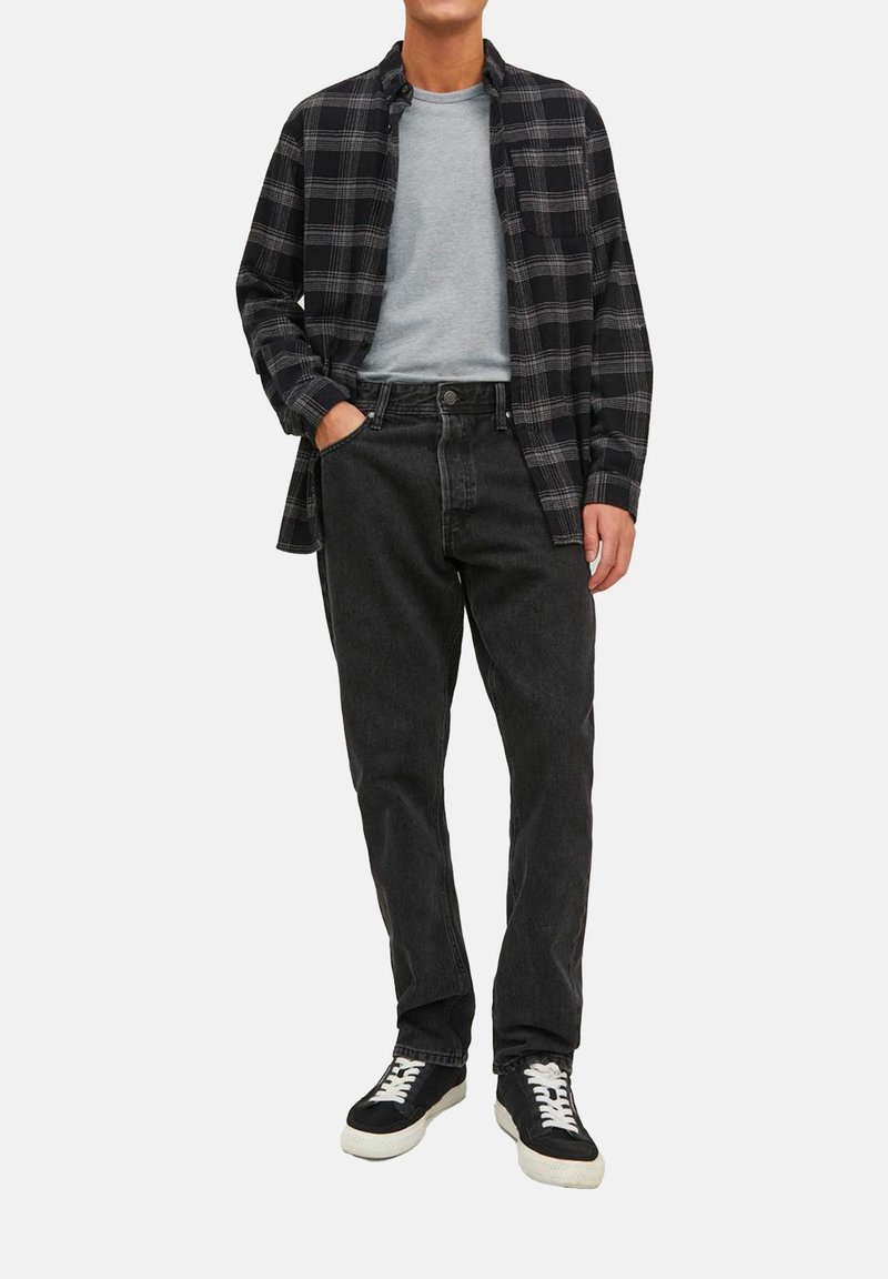 Camicia a quadri nera e grigia sopra una t-shirt grigia chiara, indossata con jeans scuri e sneakers nere con lacci bianchi.