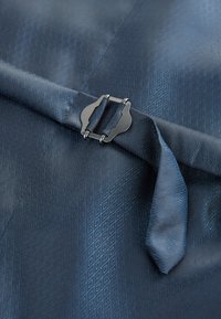 Tessuto blu scuro con un motivo geometrico sottile fissato da una piccola fibbia in metallo su una cinghia.