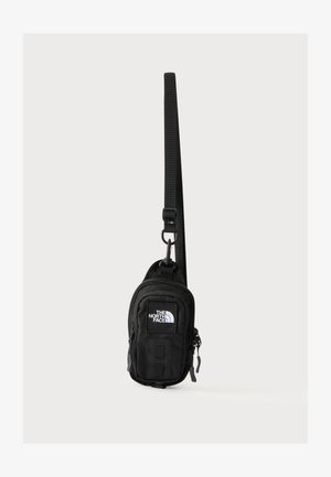 Mała czarna torebka na ramię z regulowanym paskiem i naszywką z logo The North Face z przodu, pokazana wisząca na białym tle.