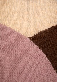 Gros plan sur un tissu tricoté avec des blocs de couleur crème, marron et rose poussiéreux formant un motif géométrique.