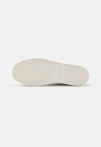 Suola di sneaker bianca con superficie texturizzata, caratterizzata da un motivo di cerchi sovrapposti e dal marchio Calvin Klein. Materiale in gomma liscia.