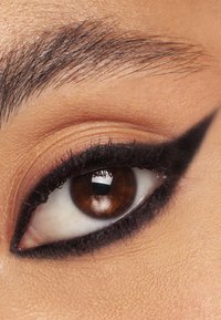 Primo piano di un occhio marrone con un eyeliner nero a code ben evidente, ciglia scure, pelle liscia e un sopracciglio scuro ben curato sopra.