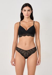 Set di lingerie in pizzo nero con un design scollato, reggiseno a scollatura profonda con spalline regolabili e mutandine in pizzo coordinate con un motivo geometrico.