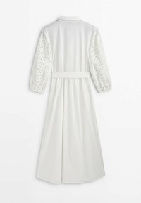 Robe blanche avec un col, des manches longues bouffantes avec des découpes en forme de feuille, et une taille cintrée avec une ceinture.