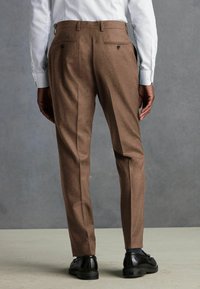 Pantalones marrones a medida hechos de tela texturizada, con dos bolsillos traseros y un diseño ajustado, combinados con zapatos de vestir negros.