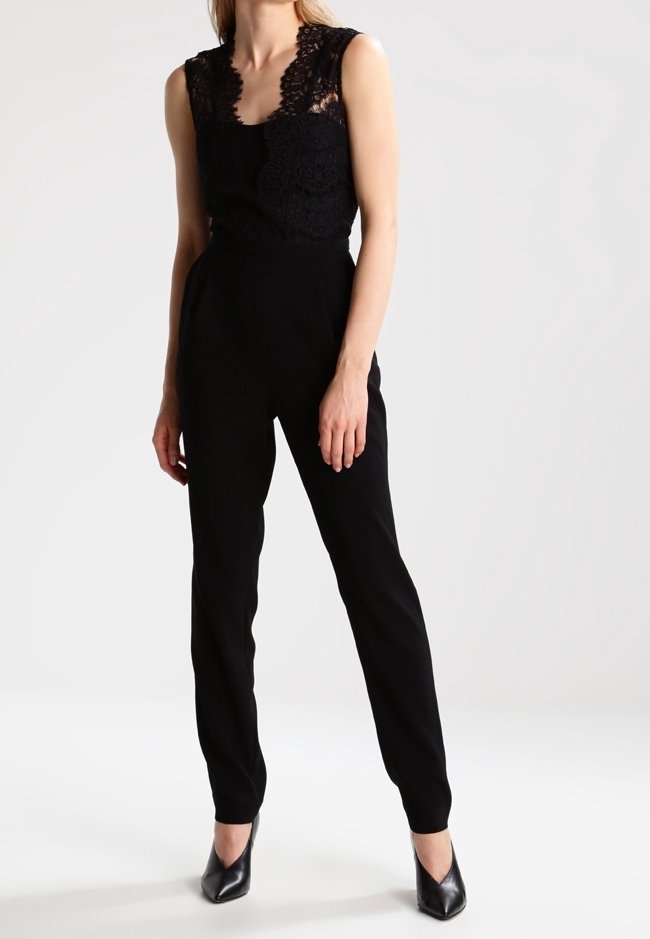 Svart jumpsuit med spetsöverdel, ärmlös design, smalnande ben och en slät textur. Matchad med spetsiga svarta klackar.