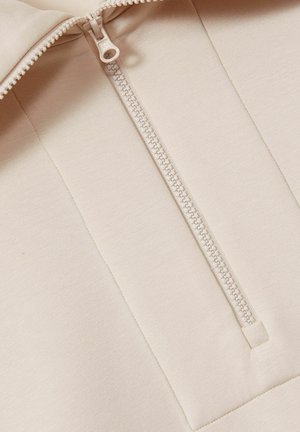Beige krāsa ar rāvējslēdzēju pulovers, kas izgatavots no gludas, elastīgas auduma, ar augstu apkakli un centrālo šuvi ar kontrastējošu rāvējslēdzēja detaļu.