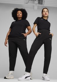 Zwarte sportieve polo's en joggers van vochtregulerende stof, met contrasterende accenten en zakken. Witte sneakers maken de outfits compleet.