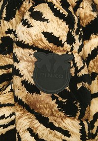Veste matelassée rayée tigre en noir et beige avec un patch circulaire noir sur la poitrine comportant deux oiseaux et le mot « PINKO ».