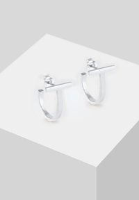 Cercei din argint în formă de inel, cu un design geometric în formă de T. Textură netedă cu un finisaj lustruit și cleme de siguranta tip buton.