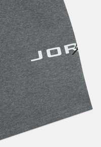 Šedé bavlnené tričko s veľkým bielym logom "JORDAN". Mäkká textúra, krátke rukávy a rovný lem.