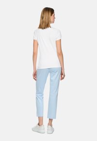 White short-sleeve t-shirt paired with light blue cropped trousers and white sneakers, featuring subtle hardware accents on the shoes.