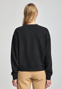 Svart sweatshirt med sänkta axlar, ribbad mudd och nederkant. Enkelt mönster, inga tryck. Matchas med beiga byxor.