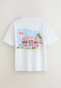 T-shirt blanc avec une illustration colorée d'un diner rétro avec une porte rouge, des tabourets extérieurs et des panneaux indiquant burgers, hot-dogs et milkshakes.
