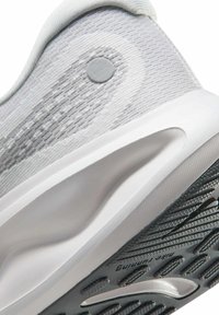 Zapatilla deportiva gris con parte superior de punto texturizado, talón redondeado y una media suela blanca. Presenta un acento circular gris en el costado.