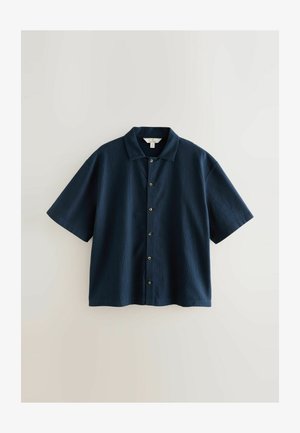 Tmavě modrá košile s krátkým rukávem a límečkem, s texturovanou tkaninou, zapínáním na knoflíky v přední části a zakulaceným lemem.