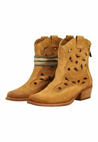 Botines de ante color beige con patrones calados, tacones bajos apilados de madera y detalle de tela a rayas alrededor del empeine de una bota.