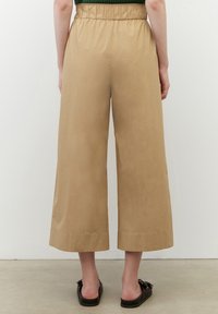 Tan vida byxor gjorda av mjukt tyg; har ett elastiskt midjeband och är avkortade i längden. Platt fåll utan synliga mönster eller detaljer.