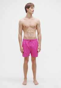 Ροζ μαγιό σορτς από ελαφρύ υλικό με ελαστική μέση και κορδόνι, με μονόχρωμο σχέδιο και μήκος μέχρι το γόνατο.