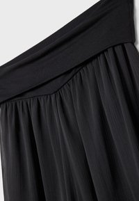 Schwarzer plissierter Rock mit einem breiten, glatten Taillenband aus einem weichen Stoff. Verfügt über eine leichte, fließende Textur und durchgehende vertikale Streifen.