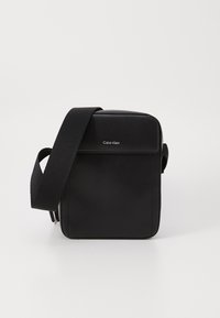 Bolso cruzado de cuero negro con correa ajustable, que presenta una tapa frontal plana, un logo discreto y un diseño rectangular elegante.
