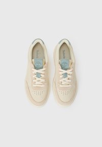Beige sneakers laget av skinn og semsket skinn. Har dekorative perforeringer, kremfargede snørebånd, og en blå vekt på tungen.