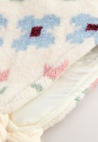 Gestrickte Decke aus weicher Wolle mit cremefarbenem Grund, verziert mit einem mehrfarbigen Muster aus blauen, roten und grünen Formen sowie einer strukturierten Oberfläche.