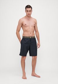Calções de banho pretos com uma cinta decorativa com um padrão de motivo grego. Material leve, design até aos joelhos e ajuste casual. Sem bolsos.