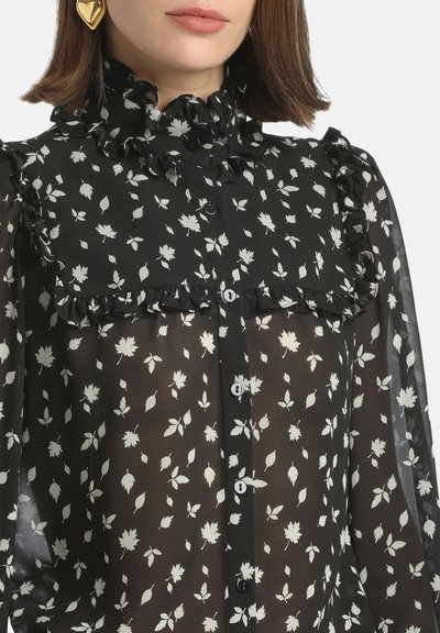 Black sheer blouse with white leaf pattern. Features ruffled high collar and yoke, with buttons down the front. Long sleeves with ruffle accents.