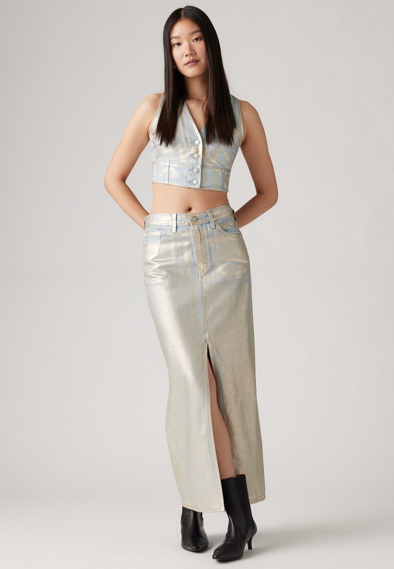 Metallic silberne, verkürzte Weste mit Knöpfen, kombiniert mit einem passenden Rock mit einem vorderen Schlitz, getragen mit schwarzen Stiefeletten.