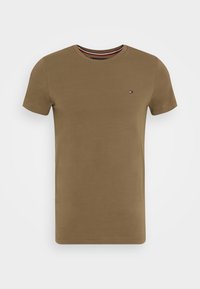 Ruskea puuvillainen T-paita, jossa on lyhyet hihat, pyöreä pääntie ja pieni logokoristesomiste vasemmassa rinnassa. Tasainen pinta ja normaali istuvuus.